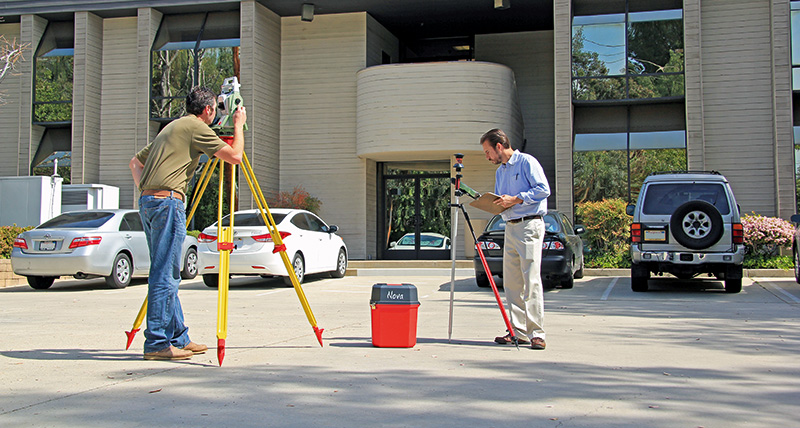 Surveying street curb for 3D model and as-built checks with Leica AP20 AutoPole and TS16 robotic total station from Leica Geosystems on construction site with bulldozer.