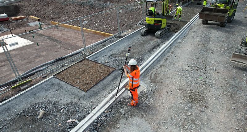 Surveying street curb for 3D model and as-built checks with Leica AP20 AutoPole and TS16 robotic total station from Leica Geosystems on construction site with bulldozer.