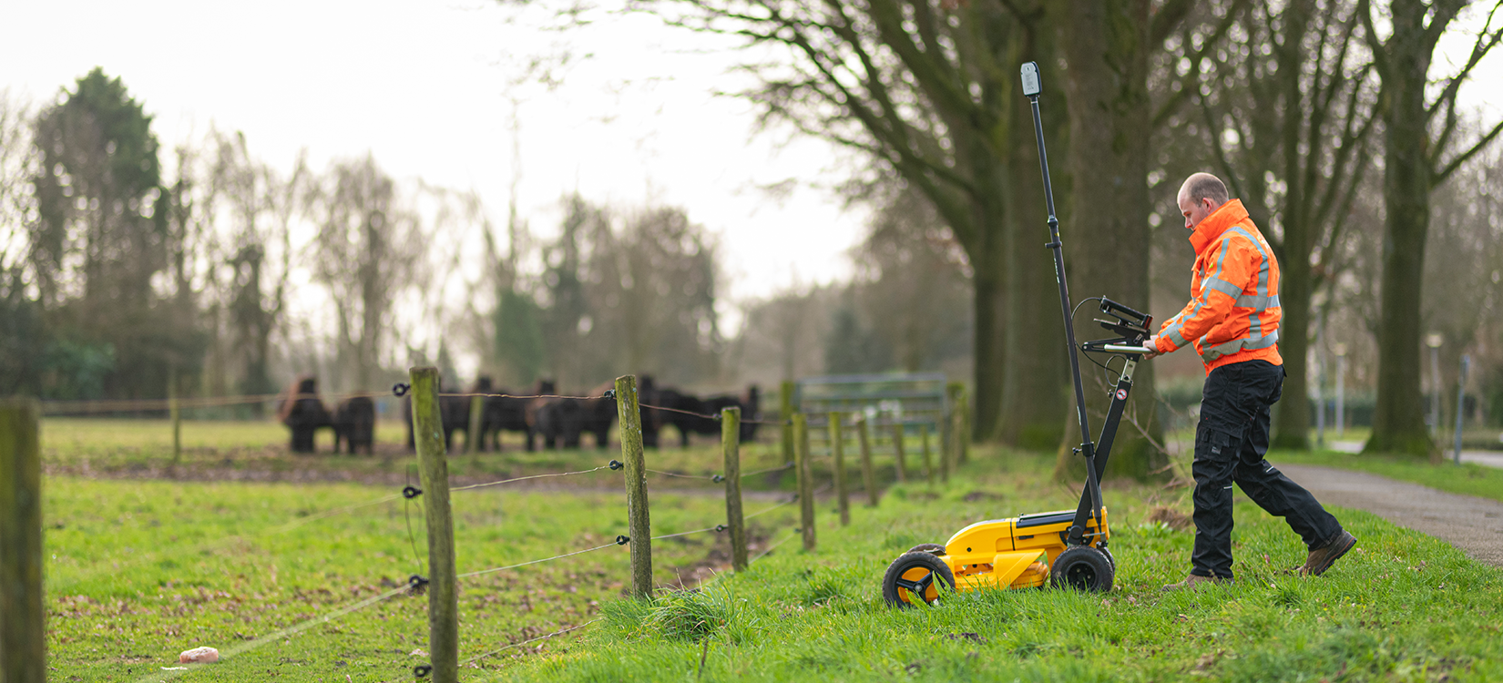 Werknemer Siers groep met Leica DS2000 grondradar in berm langs een wei met koeien