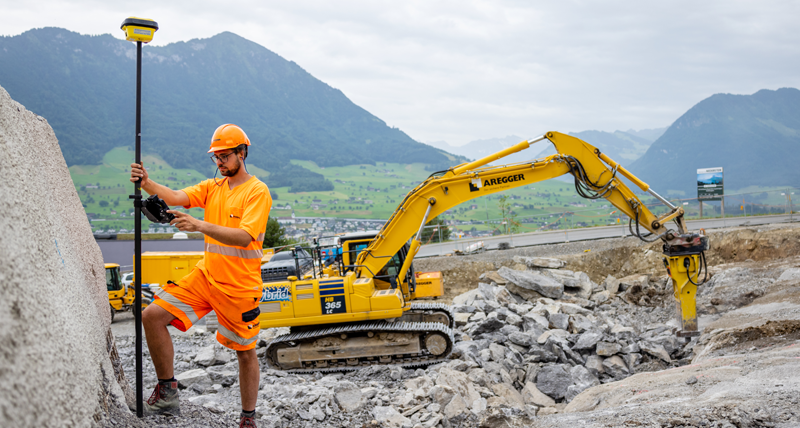 Construction worker with Leica iCON gps antenna infront of a yellow digger.