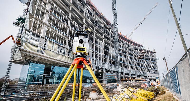 Leica iCON iCR70 construction robotic total station in front of a new buiding with construction worker in yellow vest.