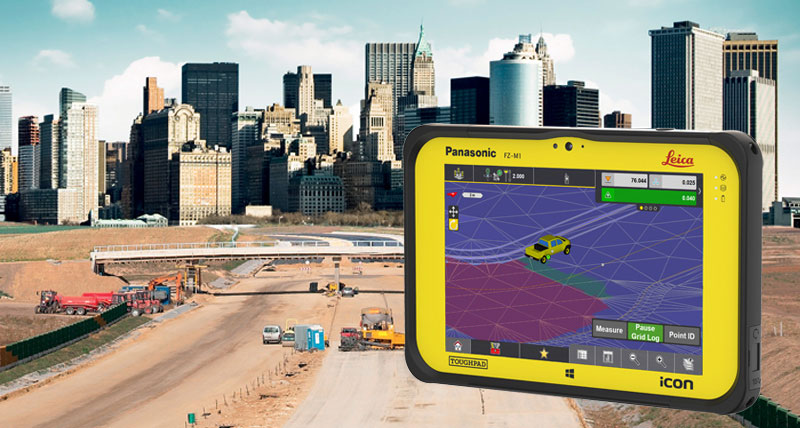 Leica iCON CC80 veldcontroller met iCON site-software met op de achtergrond een wegenbouwterrein buiten de grote stad.