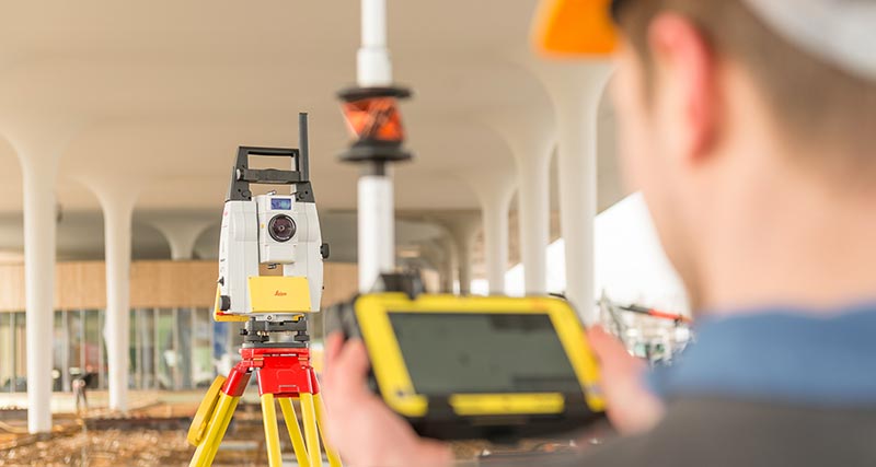 Leica iCON iCR80 sur un chantier avec un ouvrier devant l’instrument, tenant une canne à plomb avec un contrôleur de terrain CC80.
