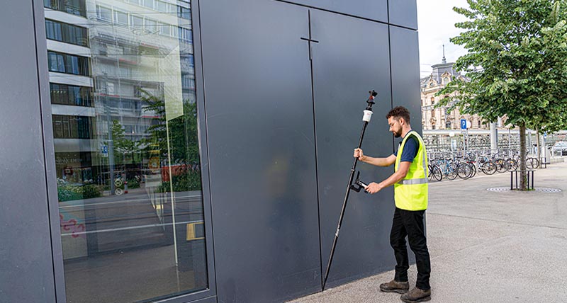 Surveyor measures points at the base of a building with a tilted AP20 prism pole for Leica robotic total stations.